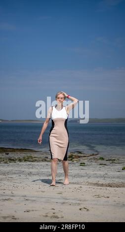 Frau in einem eleganten Kleid, die barfuß an einem Sandstrand auf den Orkney Isles, Schottland, Großbritannien, spaziert Stockfoto