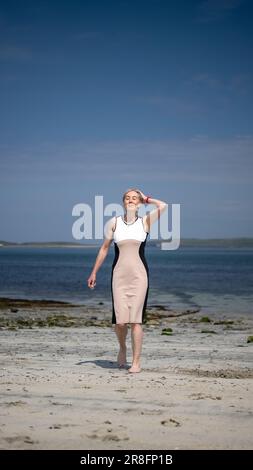 Frau in einem eleganten Kleid, die barfuß an einem Sandstrand auf den Orkney Isles, Schottland, Großbritannien, spaziert Stockfoto