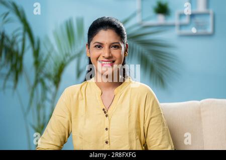Selbstbewusste, lächelnde Indianerin, die zu Hause auf dem Sofa in die Kamera schaut - Konzept von positiver Emotion, Zufriedenheit und Befähigung. Stockfoto