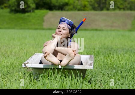 Frau sitzt in der Badewanne auf ein grünes Feld mit Gras und eine Taucherbrille an einem sonnigen Tag Stockfoto