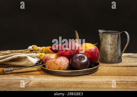 Stillleben mit Nektarinen, Paraguayas und reifen Pflaumen auf einer unbehandelten Holzfläche Stockfoto