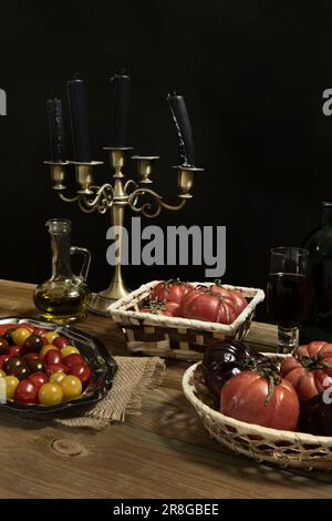 Stillleben mit Tomaten verschiedener Sorten mit etwas Olivenöl in verschiedenen Tabletts auf einer unbehandelten Holzfläche Stockfoto