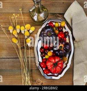 Ein ruhiges Leben mit köstlichen reifen Tomaten in einem Metalltablett neben einigen getrockneten gelben Blumen Stockfoto