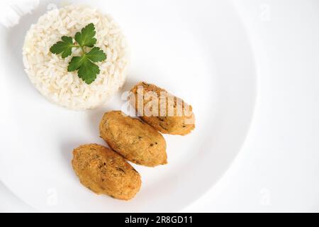 Kabeljauknödel oder „Bolinhos de bacalhau“, sehr berühmt in der portugiesischen Gastronomie. Teller mit Kabeljaugebäck serviert mit weißem Reis. Stockfoto