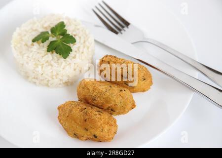 Kabeljauknödel oder „Bolinhos de bacalhau“, sehr berühmt in der portugiesischen Gastronomie. Teller mit Kabeljaugebäck serviert mit weißem Reis. Stockfoto