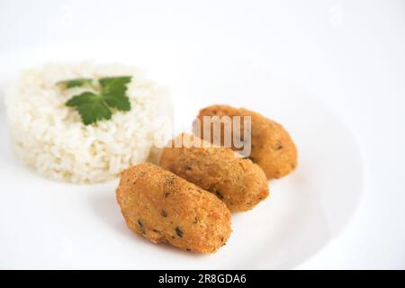 Kabeljauknödel oder „Bolinhos de bacalhau“, sehr berühmt in der portugiesischen Gastronomie. Teller mit Kabeljaugebäck serviert mit weißem Reis. Stockfoto