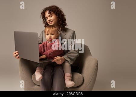 Erfolgreiche Karriere, Erfolg im Arbeitsleben, berufstätige Eltern, glückliche Geschäftsfrau mit Laptop und Sessel mit Tochter, Mutter und Kind Stockfoto