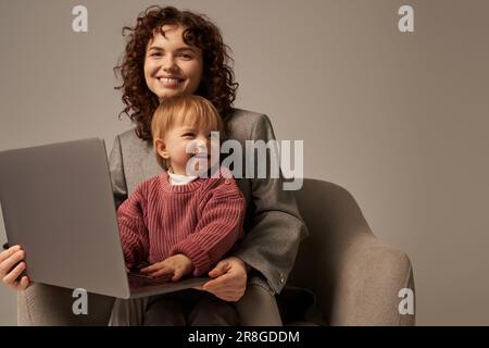 Aufbau einer erfolgreichen Karriere, ausgewogener Lebensstil, berufstätige Eltern, glückliche Geschäftsfrau, die mit ihrem Laptop und dem Sessel mit Tochter, Mutter und Chi sitzt Stockfoto