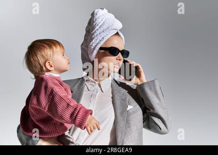 Zeitmanagement, Multitasking, Frau mit Sonnenbrille, die sich in den Armen hält, Tochter, die mit einem Handtuch auf dem Kopf steht, Geschäftsfrau in formeller Kleidung, die sich auf s unterhält Stockfoto