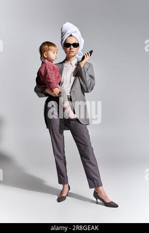 Multitasking, Frau mit Sonnenbrille, die sich in den Armen hält, Tochter und Steh mit Handtuch auf dem Kopf, ausgewogene Lebensweise, Geschäftsfrau in formeller Kleidung Stockfoto