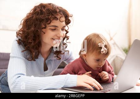 Multitasking-Frau, Freiberufler, moderne berufstätige Eltern, die Arbeit und das Leben in Einklang bringen, fröhliche Frau, die ein Notebook in einem gemütlichen Wohnzimmer benutzt, moderne Erziehung, Buil Stockfoto