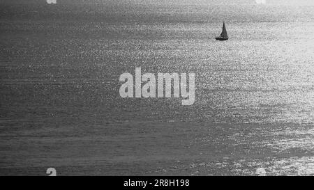 Einzelsegelboot auf ruhigem Meer in Schwarz-Weiß Stockfoto