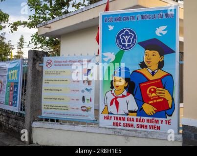 Werbe- und Propagandaposter vor einer weiterführenden Schule in Kontum, im zentralen Hochland Vietnams. Das Poster auf der linken Seite warnt Stockfoto