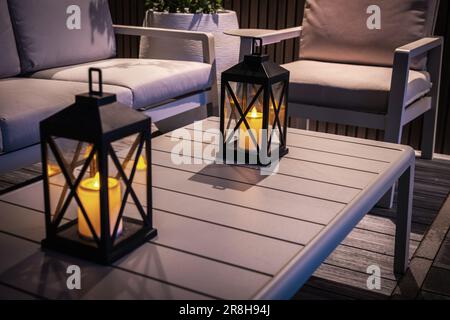 Nahaufnahme von Gartenkerzen auf dem Tisch im Freien, die die Terrasse am Abend gemütlich beleuchten. Hinterhof-Design. Stockfoto