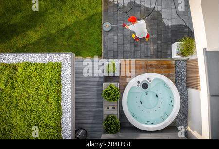 Luftaufnahme der kaukasischen Mann reinigenden Terrassenkacheln in seinem modernen Garten mit Hochdruckreiniger. Verwaltung Der Umgebung Zu Hause. Stockfoto