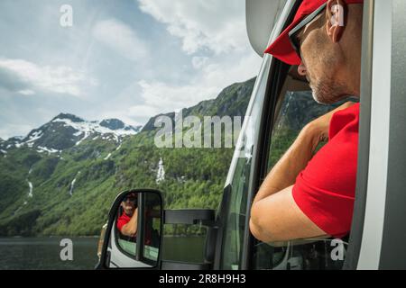 Weißer Tourist in seinen 40s Jahren, der vor seinem Wohnmobil-Fenster blickt und die Aussicht genießt. Malerische Norwegische Sommerlandschaft Stockfoto