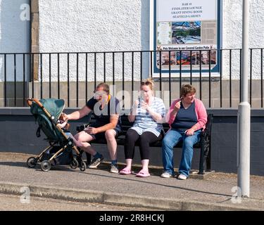 18. Juni 2023 Cullen, Moray, Schottland. Dies ist eine kleine Familiengruppe, die die Sonne aufsaugt und ein Eis isst, während sie auf einer Sitzbank sitzt. Stockfoto