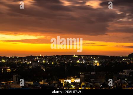 Blick auf die Stadt bei Nacht mit dramatischem orangefarbenem Sonnenuntergang vom Berggipfel am Abend Stockfoto
