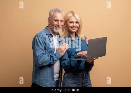 Positives älteres Paar im Ruhestand, das seinen Laptop auf beigefarbenem Hintergrund benutzte Stockfoto