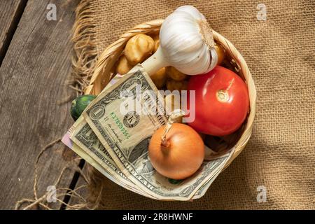 Tomatenzwiebeln Knoblauchkartoffeln in einem Korb mit Dollars auf einem Holztisch, Gemüse und Geld Stockfoto