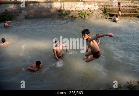 Pulwama, Indien. 21. Juni 2023. Ein Junge springt während eines heißen Tages in Pulwama, während andere im Kanal schwimmen. Die Höchsttemperatur in Srinagar stieg auf 34,0°C und lag für die Saison 4,8°C über dem Normalwert. Die Temperatur von heute überstieg die vorige Höchsttemperatur von 33,3°C, die erst gestern verzeichnet wurde, sagte der Beamte. (Foto: Idrees Abbas/SOPA Images/Sipa USA) Guthaben: SIPA USA/Alamy Live News Stockfoto