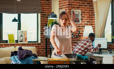 Depressive Frau, die keine Wäsche mehr bügeln will, gestresste Hausfrau, die Hausarbeiten macht. Junger Erwachsener, der traurig ist wegen der Frühjahrsputz-Reinigung und Hausarbeit allein. Stockfoto
