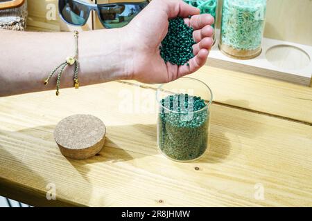 Portsmouth, Großbritannien. 20. Juni 2023. Die Hand einer Person, die während der Revolution Plastics Future Conference der University of Portsmouth in Portsmouth recycelte Plastikpellets aus verlassenen Fischernetzen eingießt, die an den Küsten von Cornwall, Newquay, gesammelt wurden. Waterhaul, ein in Großbritannien ansässiges Sozialunternehmen in Cornish, bekämpft die Plastikverschmutzung durch weggeworfene Fanggeräte, indem es diese in recycelte Sonnenbrillen umwandelt. Die internationale Plastics Future Conference wurde veranstaltet, um globale Forschung und Innovation über verschiedene Disziplinen und Gemeinschaften hinweg auszutauschen, um das Problem der globalen Kunststoffverschmutzung anzugehen Stockfoto