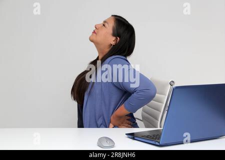 40-jährige Latina-Frau leidet unter Rücken-, Nacken- und Kopfschmerzen aufgrund von Stress und Burnout, während sie mit ihrem Laptop in ihrem Büro arbeitet Stockfoto