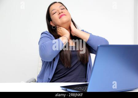 40-jährige Latina-Frau leidet unter Rücken-, Nacken- und Kopfschmerzen aufgrund von Stress und Burnout, während sie mit ihrem Laptop in ihrem Büro arbeitet Stockfoto