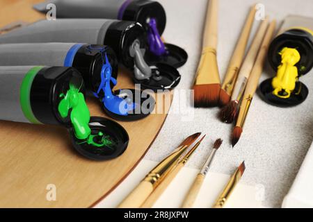 Tuben mit bunten Farben und Pinseln auf einem strukturierten Tisch, Nahaufnahme Stockfoto