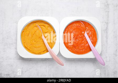 Behälter mit gesunder Babynahrung und Löffel auf weißem strukturiertem Tisch, flach liegend Stockfoto