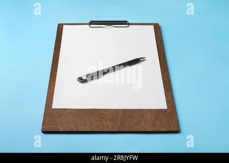 Neues Holzclipboard mit leerem Blatt Papier und Stift auf hellblauem Hintergrund Stockfoto