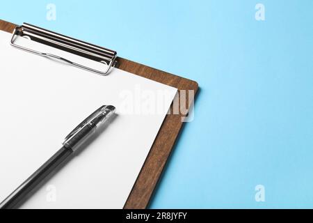 Neues Holzclipboard mit leerem Blatt Papier und Stift auf hellblauem Hintergrund. Platz für Text Stockfoto