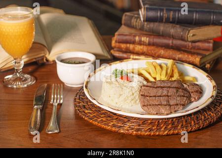 Wunderschönes Gericht mit Reis, Bohnen und gegrilltem Fleisch. Im Hintergrund alte Bücher Stockfoto