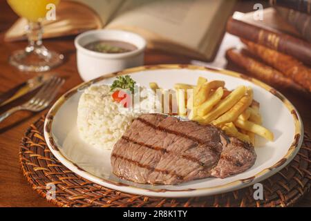 Wunderschönes Gericht mit Reis, Bohnen und gegrilltem Fleisch. Im Hintergrund alte Bücher Stockfoto