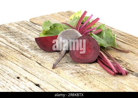 Roh geschnittene und ganze Rote Bete mit grünen Blättern auf grauem rustikalem Holzhintergrund Stockfoto