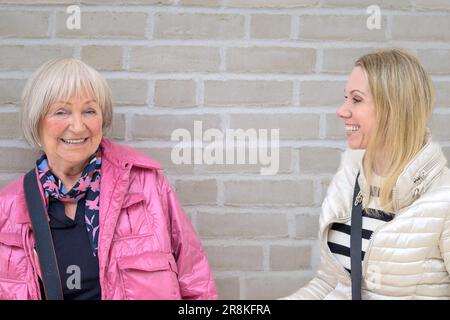 Mutter und Tochter stehen vor einer weißen Wand, während sie heftig lachen Stockfoto