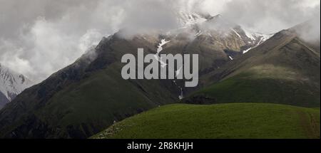 Bergpanorama. Berggipfel in den Wolken, eine Bergwiese, ein Wasserfall in einer Bergschlucht. Stockfoto