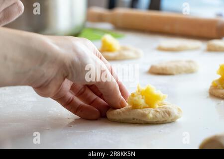 Der Prozess der Herstellung von Kuchen mit Kartoffeln zu Hause in der Küche auf einem weißen Tisch, hausgemachte Gewohnheiten mit Kartoffeln Stockfoto