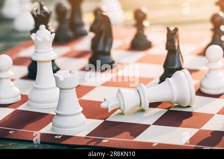 Der besiegte König liegt auf dem Schachbrett neben anderen schwarz-weißen Schachfiguren. Das Konzept der Revolution, der politischen Führung und des Sieges Stockfoto