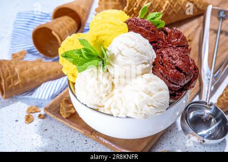 Zitronen-, Schokolade- und Vanilleeis. Große Schüssel mit Eisschaufeln, auf weißem Küchentisch-Hintergrund mit Waffelkegeln, Kopierfläche Stockfoto