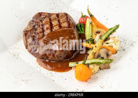 Gegrilltes Rinderfilet mit Demi-Glace-Sauce mit gegrilltem Gemüse auf einem weißen Porzellanteller Stockfoto