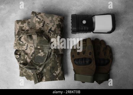 Taktische Handschuhe, Camouflage-Jacke und Campinglaterne auf hellgrauem Hintergrund, flach liegend. Militärische Trainingsausrüstung Stockfoto