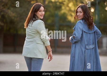 Zwei Frauen schauen zurück in die Kamera, während sie einen Spaziergang in einem Park im Freien genießen. Stockfoto