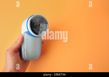 Eine Frau hält einen modernen Rasierer mit Stoff auf blassorangefarbenem Hintergrund, Nahaufnahme. Platz für Text Stockfoto