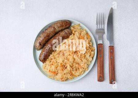 Teller mit Sauerkraut und Würstchen auf einem hellen Tisch, flach liegend Stockfoto