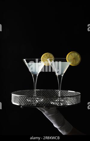 Der Kellner hielt ein elegantes Tablett mit martini-Gläsern mit frischem Cocktail vor schwarzem Hintergrund, Nahaufnahme Stockfoto