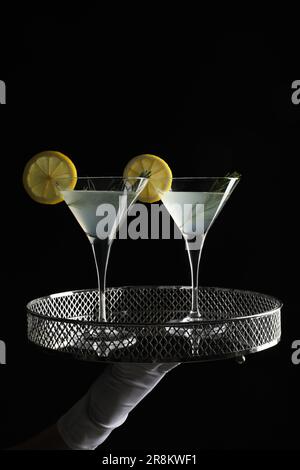 Der Kellner hielt ein elegantes Tablett mit martini-Gläsern mit frischem Cocktail vor schwarzem Hintergrund, Nahaufnahme Stockfoto