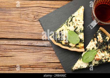 Stücke köstlicher hausgemachter Spinat-Quiche und Tee auf Holztisch, flach liegend. Platz für Text Stockfoto