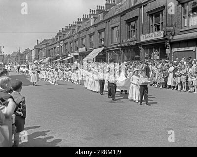 Eine Whit Walks-Prozession in Union Street, Oldham, Greater Manchester, Lancashire, England, UK c.1960. Hier stehen Kinder im Mittelpunkt der Parade mit Mädchen, die Hauben tragen. Eine „Königin“ mit einem Mädchen, das ihre Krone trägt, steht an der Spitze. Die religiöse Veranstaltung in der Church of England fand traditionell am Whit Friday statt, an dem Kinder zusammen mit Messingbändern und Silberbändern beteiligt waren. Manchester hatte die größten Whit Walks, aber andere Whit Walks waren besonders im Nordwesten Englands beliebt. White Walks in Manchester findet jetzt am Spring Bank Holiday Monday statt – ein klassisches 1950er/60s-Foto. Stockfoto